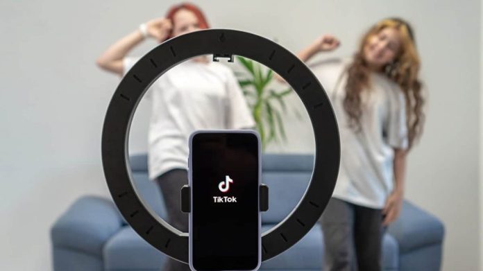 Duas meninas dançando enquanto celular com TikTok aberto e encaixado numa ring light grava