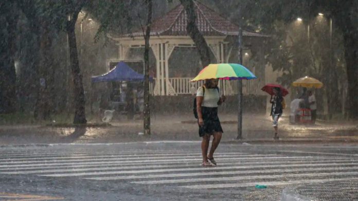 Mulher atravessando avenida de guarda-chuva durante temporal em São Paulo