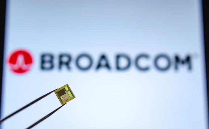 Chip segurado por uma pinça com o logotipo da BROADCOM na tela ao fundo.