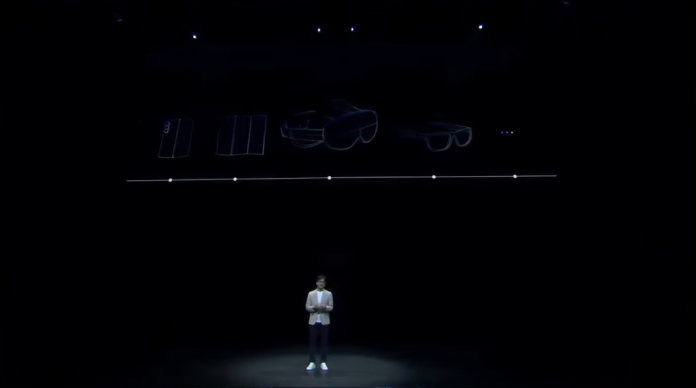 Ao fundo, em um telão, detalhe do headset e do futuro smartphone dobrável em três partes da Samsung; À frente, um executivo da empresa falando