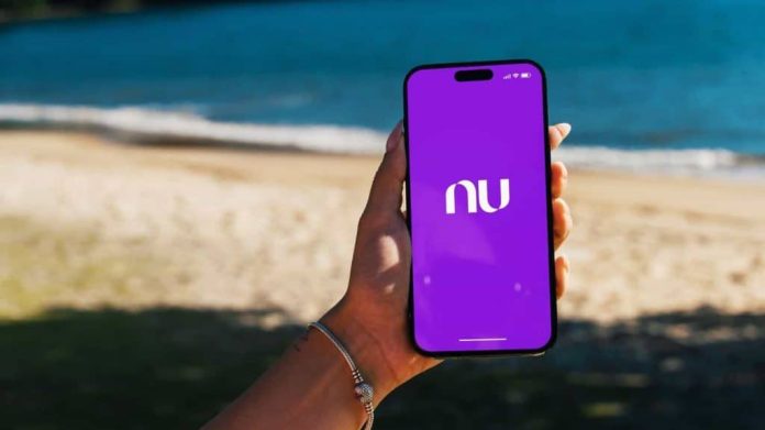 Garota na praia segurando um smartphone iPhone 14 Pro com o aplicativo do Nubank na tela. Rio de Janeiro, RJ, Brasil. 07 de junho de 2023.