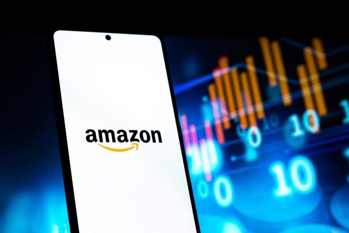 Atrás, desfocados, gráficos financeiros; à frente, logo da Amazon na tela de um smartphone