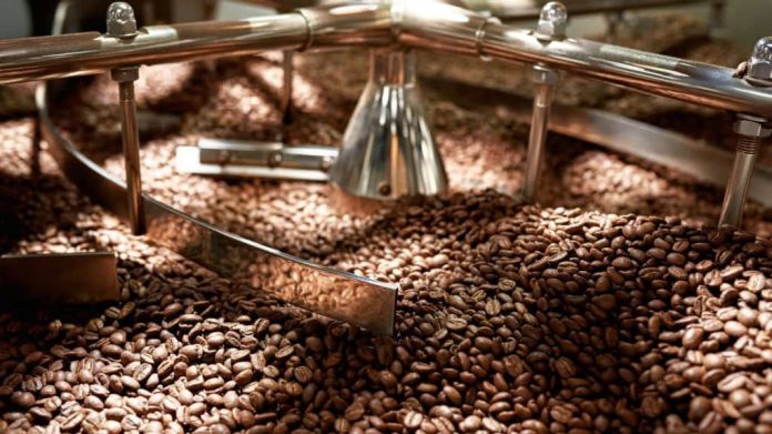 Grãos de café torrados naturalmente misturando-se no misturador da máquina de torrefação industrial na fábrica.