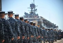 Imagem mostra marinheiros e fuzileiros navais dos EUA designados para o navio de assalto anfíbio Pre-Commissioning Unit America (LHA 6) marcham em direção ao navio no píer da Huntington Ingalls Industries em Pascagoula.