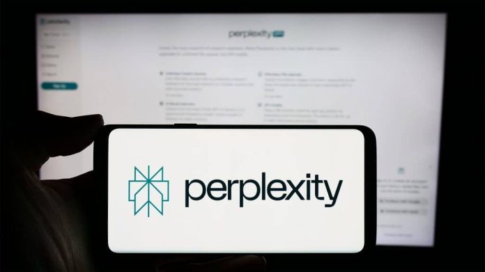 Pessoa segurando celular com logotipo do Perplexity e o buscador aberto num computador ao fundo