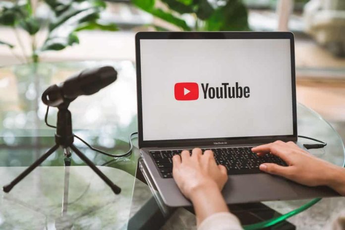 Do lado esquerdo, um microfone; do lado direito, uma pessoa mexendo em um notebook com o logo do YouTube em sua tela