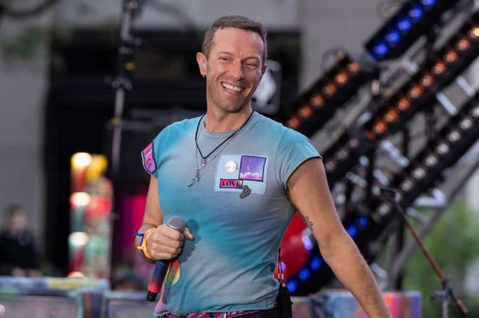 Chris Martin sorrindo, com um microfone na mão, durante uma apresentação do Coldplay