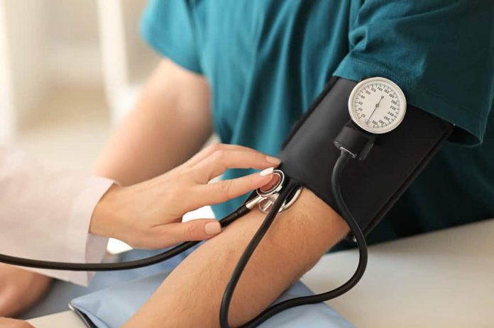 Profissional de saúde mede pressão arterial com esfigmomanômetro manual no braço de um paciente.