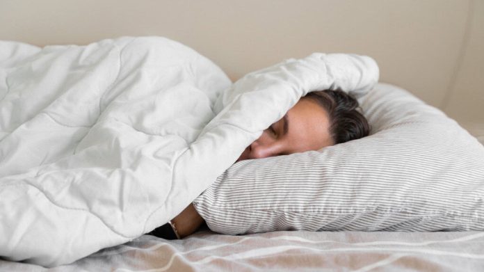 Mulher jovem da geração millennial dormindo coberta com cobertor. Inverno frio. Sem aquecimento em casa. Ronco alto. Sonhos doces. Ciclos circadianos.