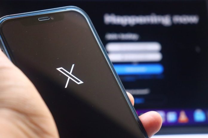 Ao fundo, desfocado, página de login do X; à frente, logo do X em um smartphone