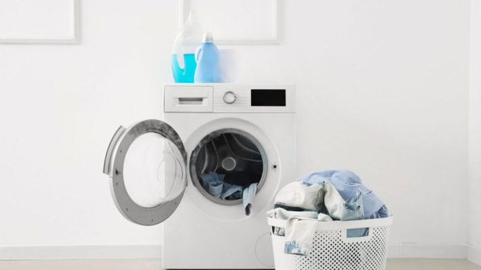 Máquina de lavar com produtos na parte de cima e um cesto de roupas sujas. A máquina está com a tampa aberta.