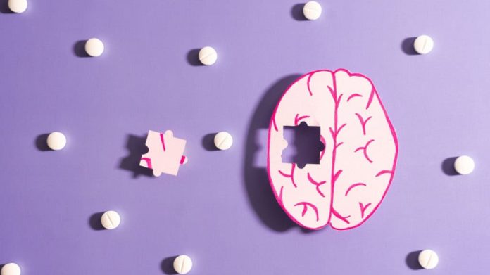 Anatomia do cérebro humano sem uma peça de quebra-cabeça com comprimidos de remédio em fundo roxo. Conceito de tratamento para Alzheimer, demência e doença de Parkinson. Cuidados com a saúde mental.